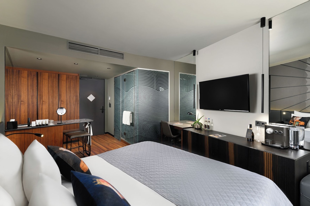Una habitación de hotel moderna con una cama grande, un escritorio con computadora, televisor y minibar.