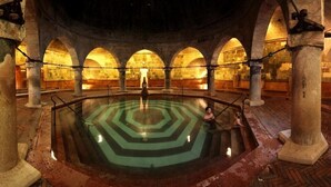 Un edificio histórico con una piscina central, columnas de piedra y techos abovedados.