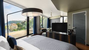 A modern hotel room with a large bed, a flat-screen TV, a desk with a chair, and a view of a cityscape.