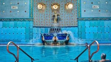 A large indoor pool with ornate blue tiles and a central fountain.