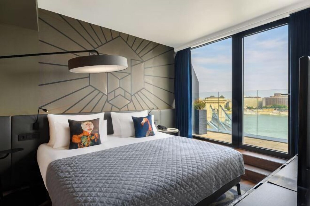 Una habitación de hotel moderna con una cama grande, vistas a la ciudad y un diseño geométrico en la pared.