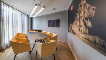 A conference room with a long table, yellow chairs, a mounted TV, and a large lion mural on the wall.