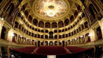 A grand theater with multiple balconies, ornate ceiling, and red seating.