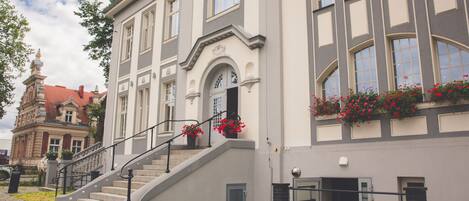 Un bâtiment avec un escalier menant à une porte, un sol pavé et une jardinière rouge sur le côté droit.