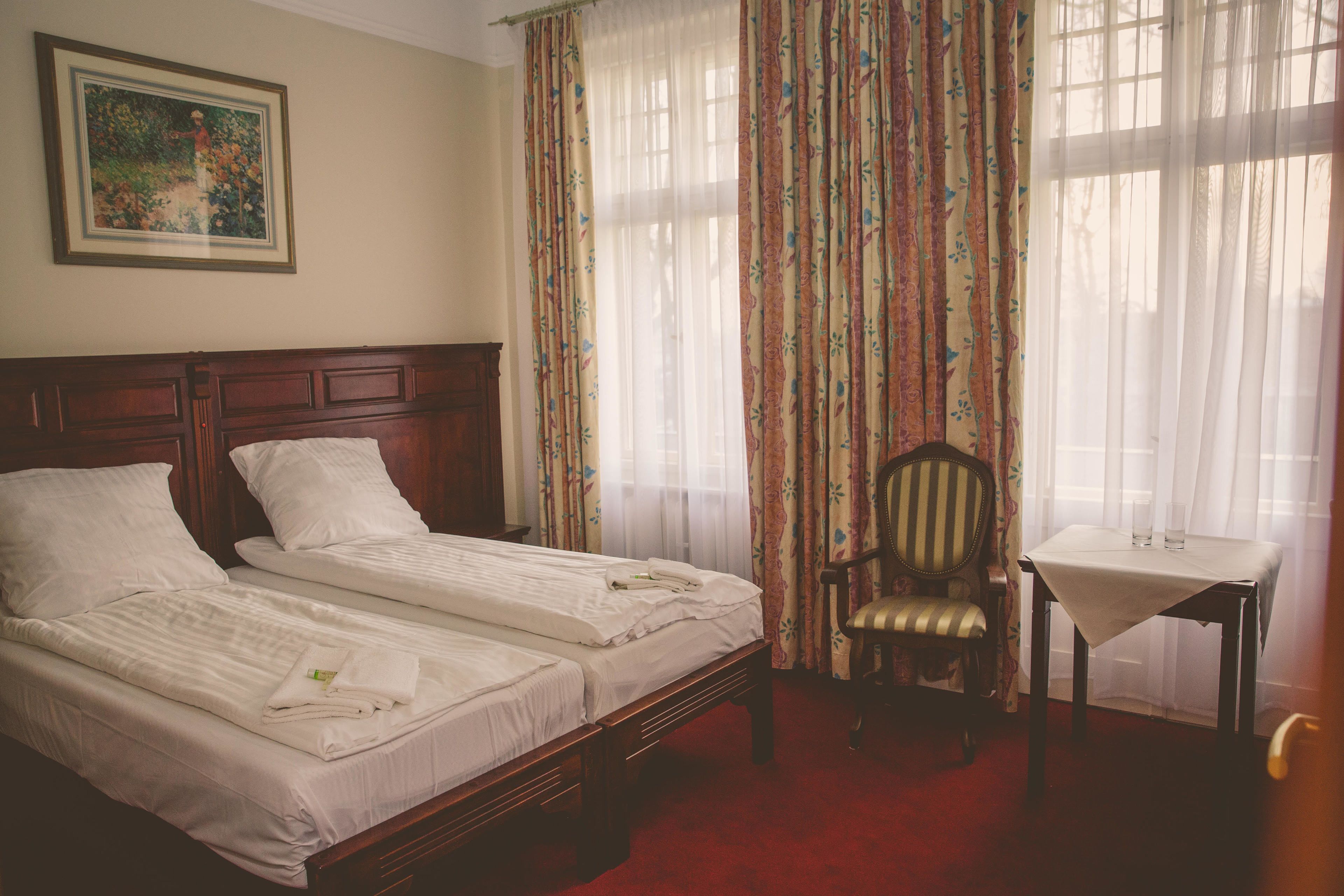 Ein Hotelzimmer mit zwei Betten, einem Sessel, einem kleinen Tisch und Vorhängen.