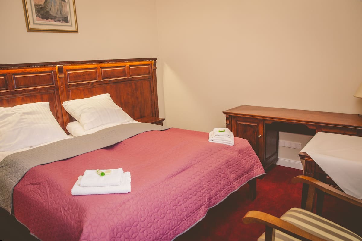 A neatly made bed with a pink quilt, white pillows, and a folded towel on the side.