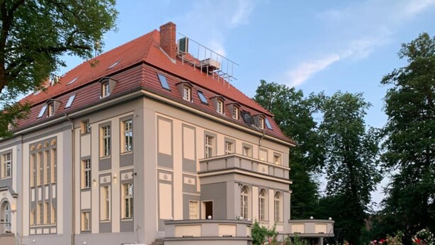 A large, historic building with a red roof and symmetrical facade, surrounded by lush gardens and blooming roses. - Hotel Willa Starosty (Miedzyrzecz)
