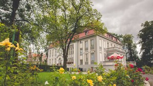 A historic building with a red roof, surrounded by a well-maintained garden with various flowers and a stone pathway. - Hotel Willa Starosty (Miedzyrzecz)