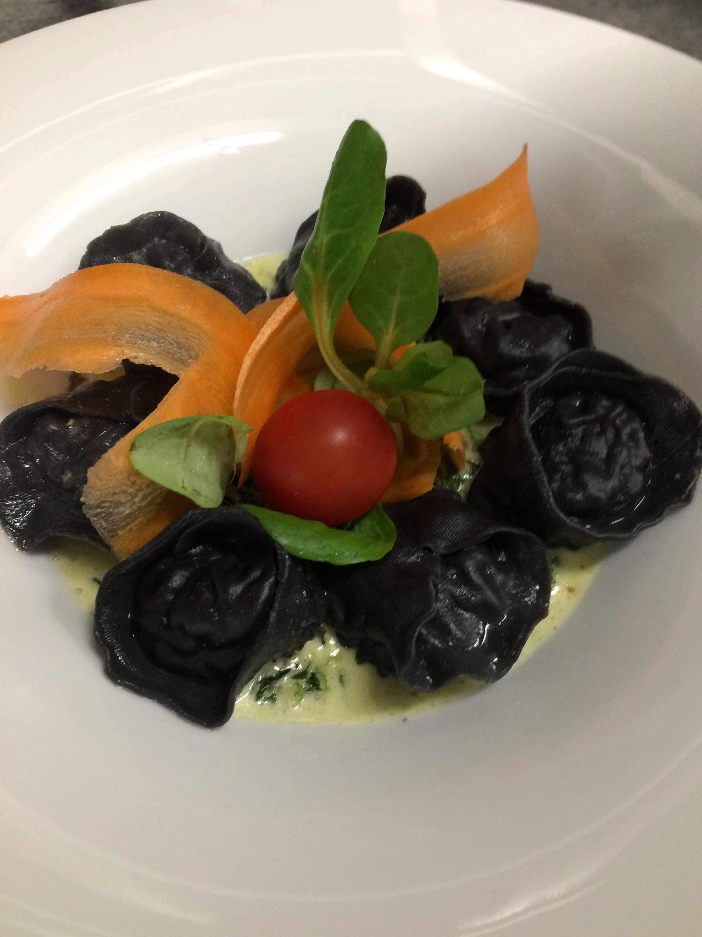 Un plato de comida con pasta negra, un tomate cherry y hojas verdes.