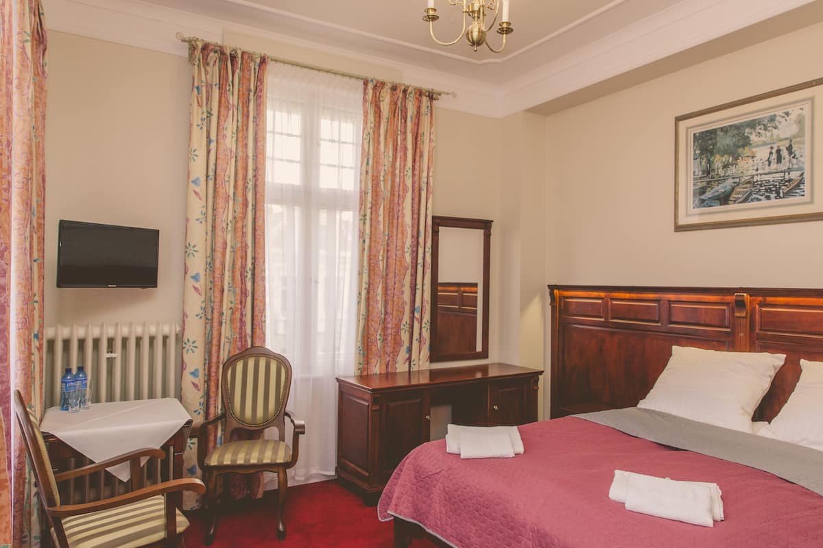 A hotel room with a bed, a desk, a chair, a dresser, a television, and a painting on the wall.