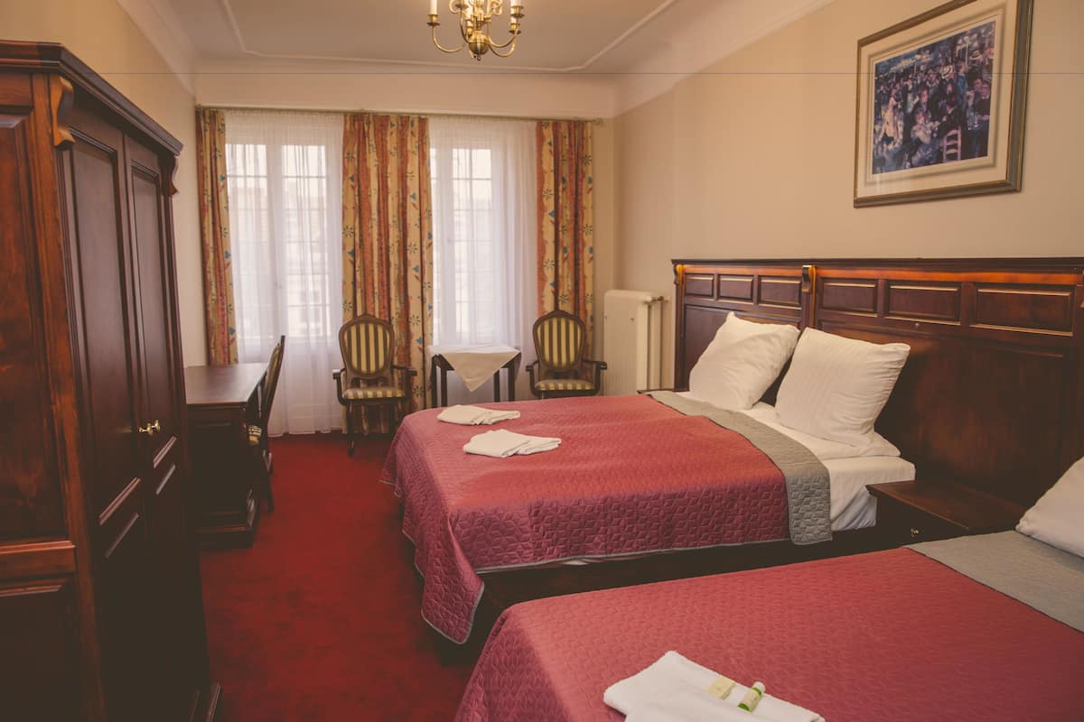 A hotel room with two beds, a desk, a chair, and a radiator.