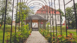 A garden pathway with a metal archway leading to a building with a red roof. - Hotel Willa Starosty (Miedzyrzecz)