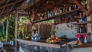 A wooden bar with shelves of bottles, a pineapple, and a fruit bowl. - Zanzibar Magic Boutique Hotel (Matemwe)