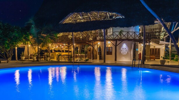 A poolside area with a thatched roof structure, a bar, and a pool reflecting the lights. - Zanzibar Magic Boutique Hotel (Matemwe)