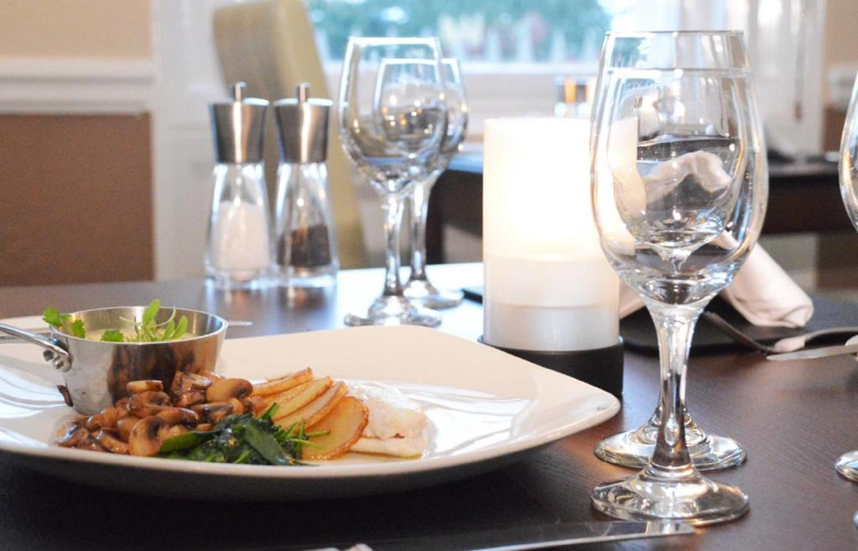 A dining table with a white plate of food, a candle, and wine glasses.