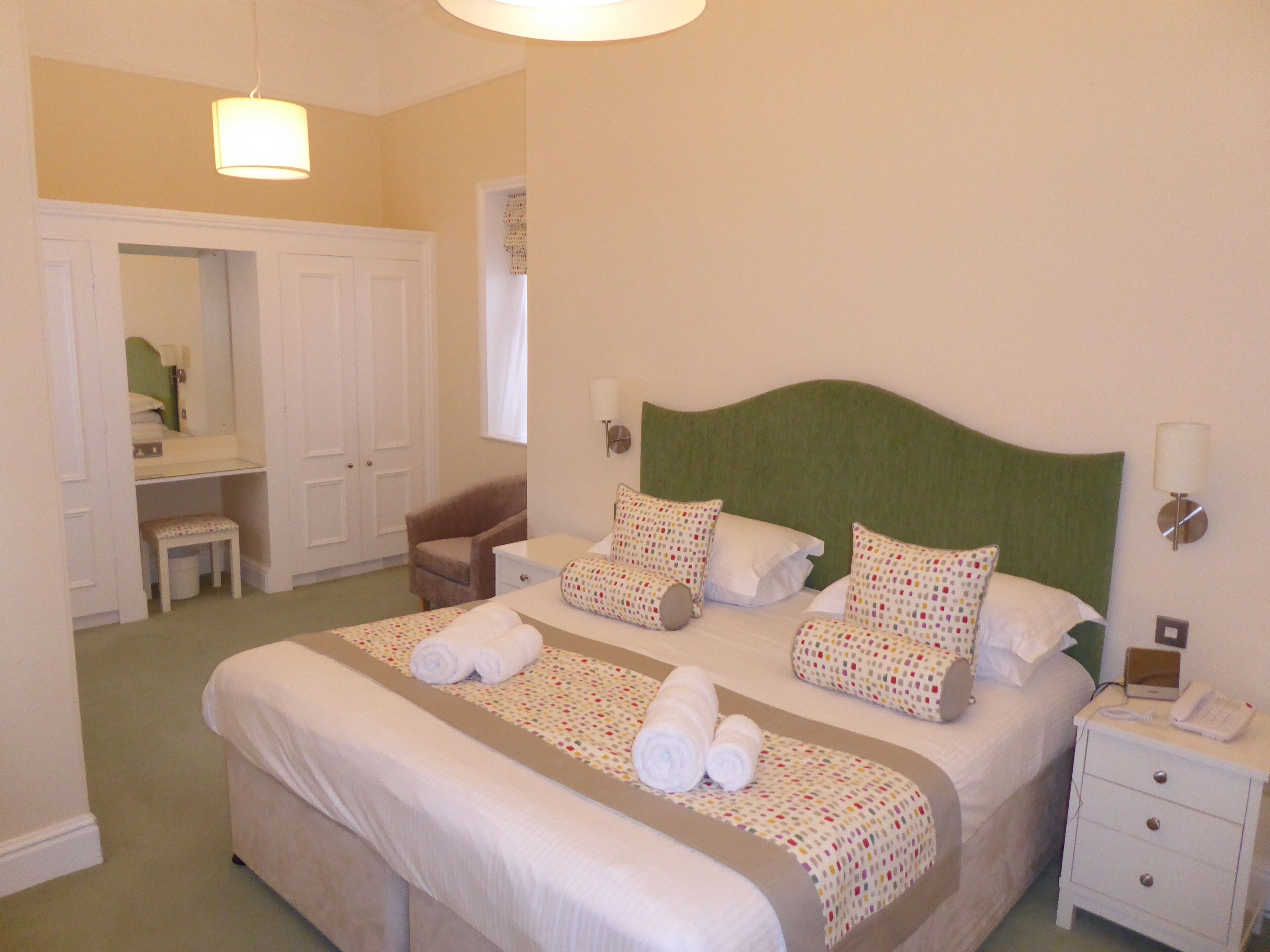 A neatly arranged bedroom with a large bed, bedside tables, a chair, a desk, and a wardrobe.
