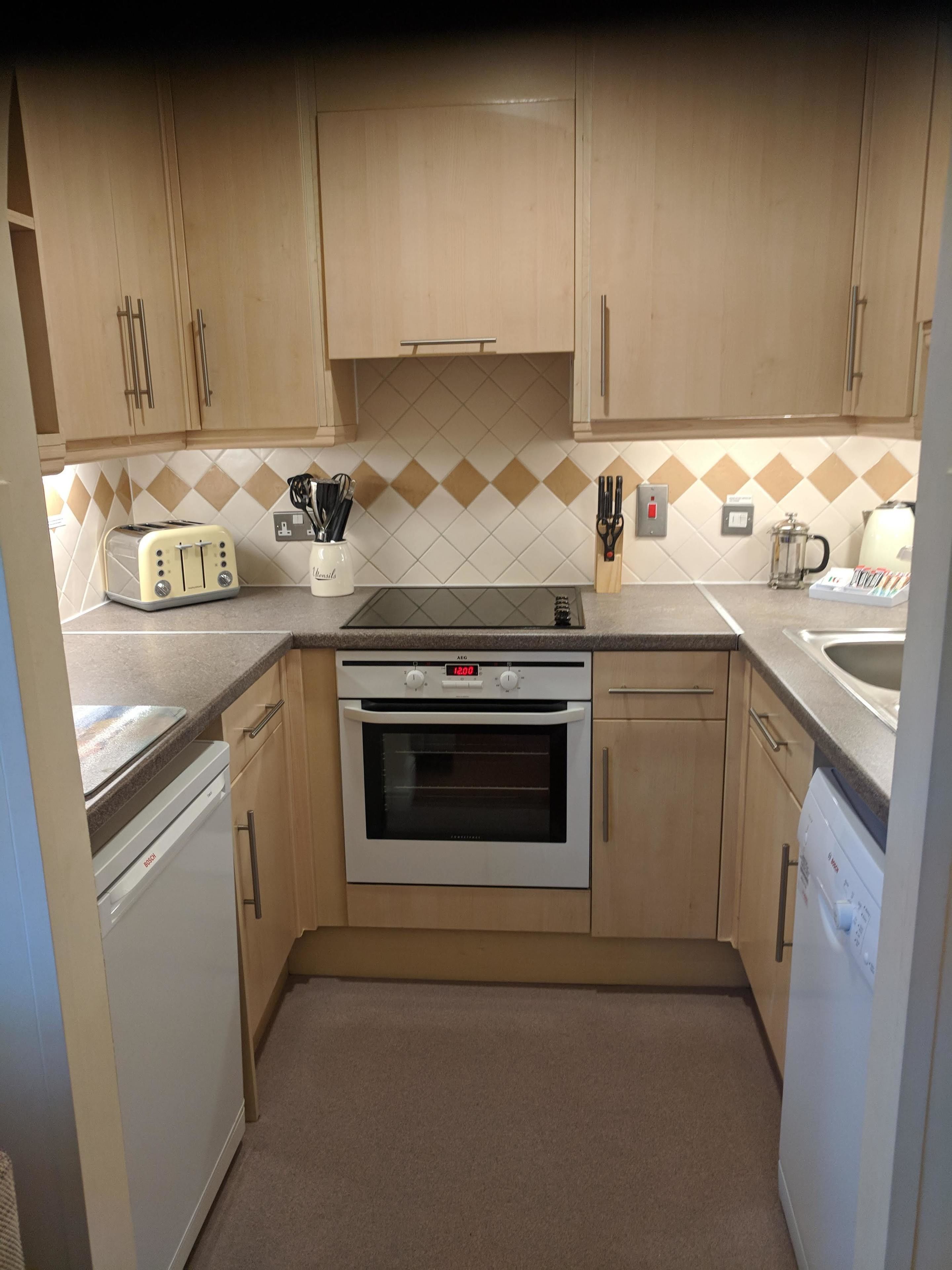 A compact kitchen with wooden cabinets, a built-in oven, a toaster, and a coffee maker.
