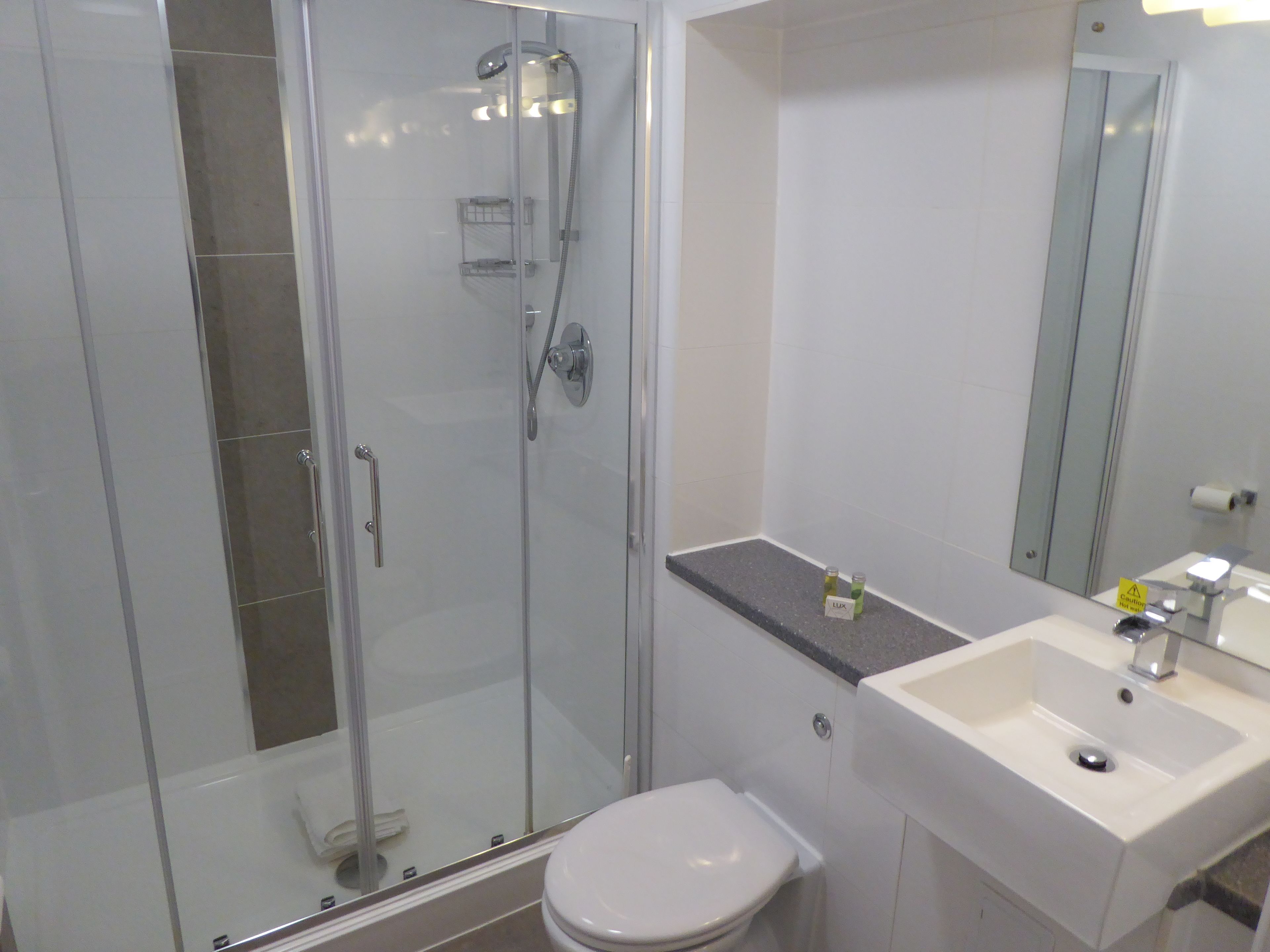 Une salle de bain moderne avec une douche à parois de verre, des toilettes blanches et un lavabo avec un miroir.