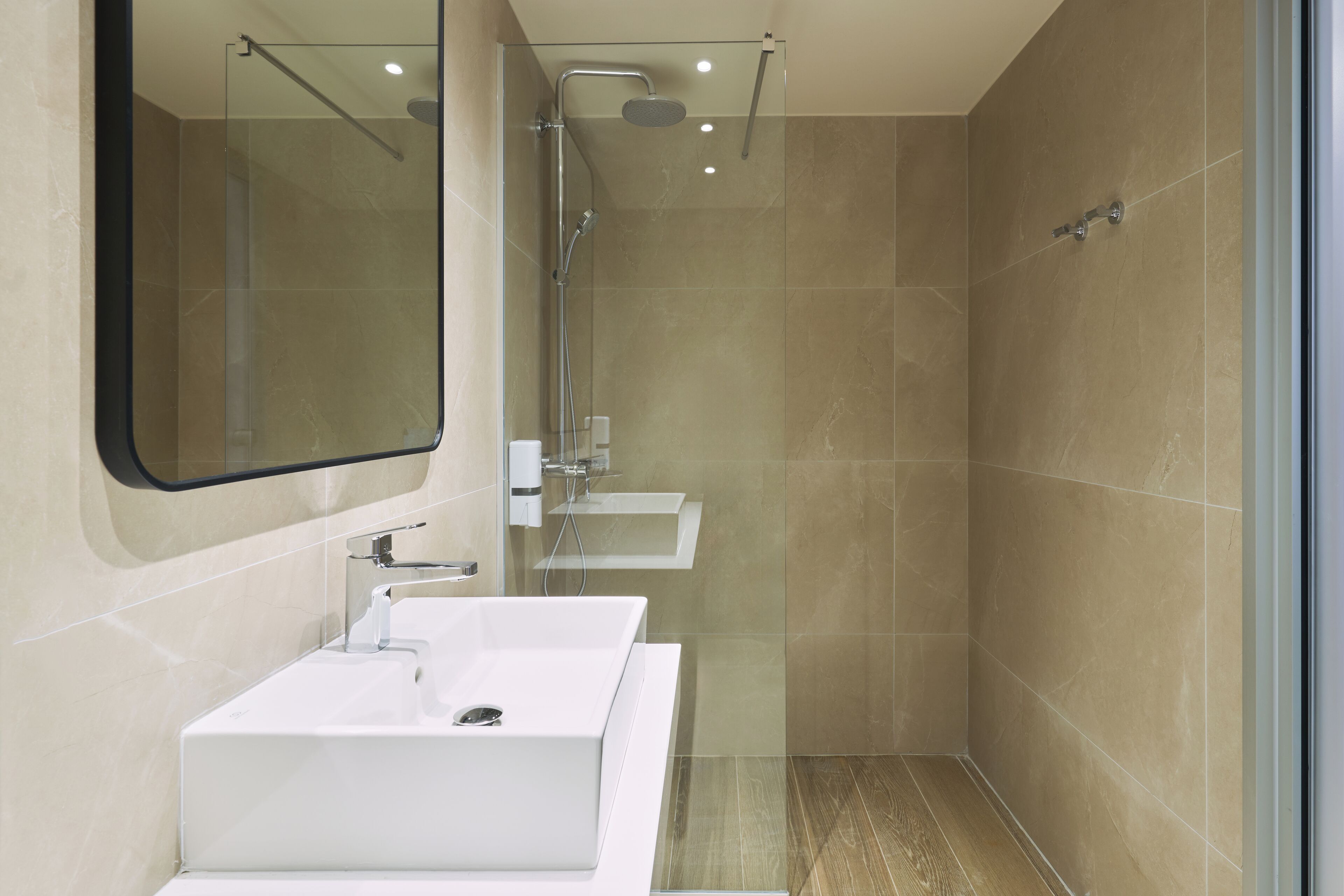 A modern bathroom with a large mirror, a white sink, and a shower area.