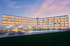 Un hotel de varios pisos con piscina, tumbonas y sombrillas.