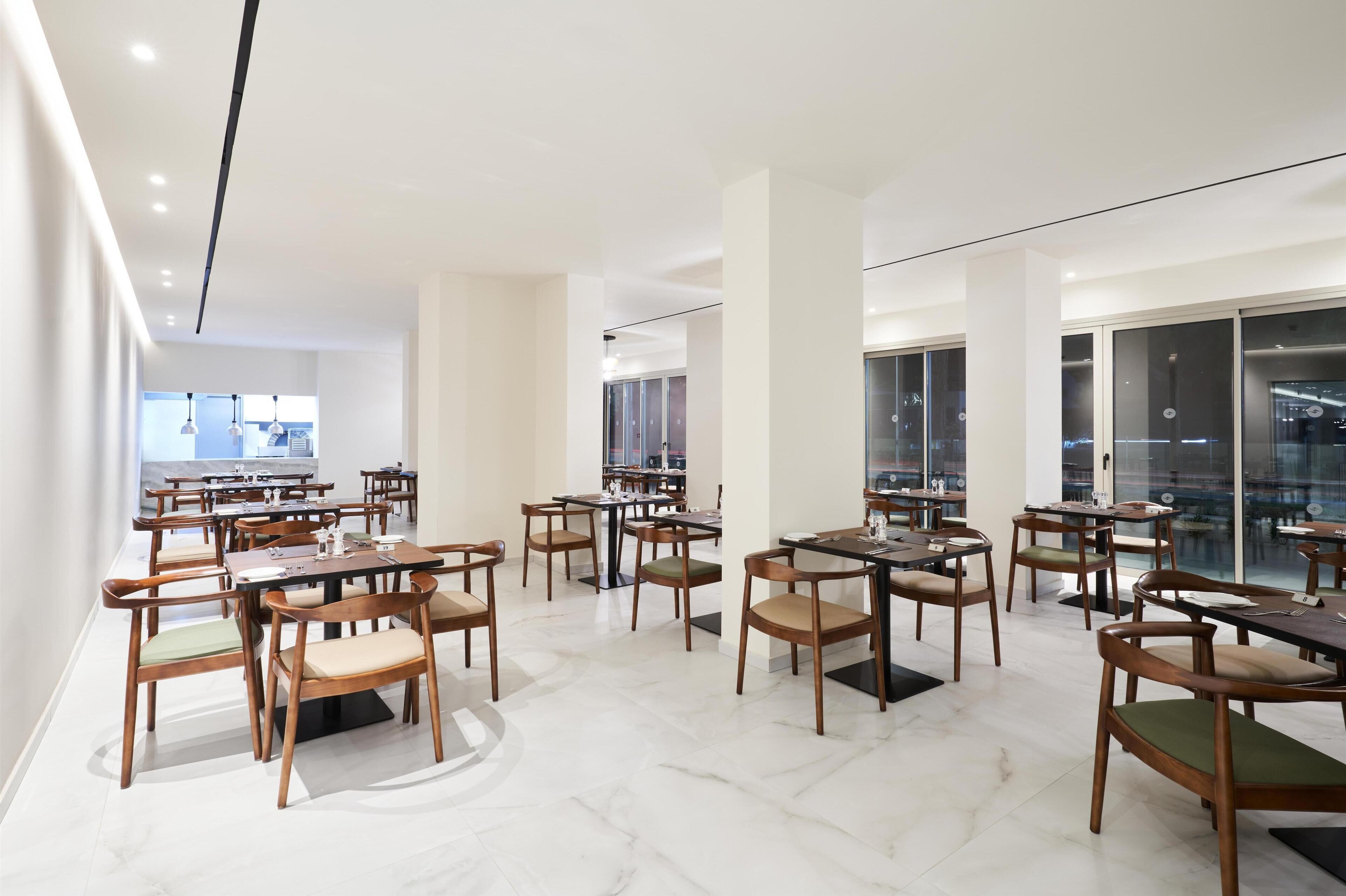 A modern dining area with wooden tables and chairs, large windows, and a clean, minimalist design.