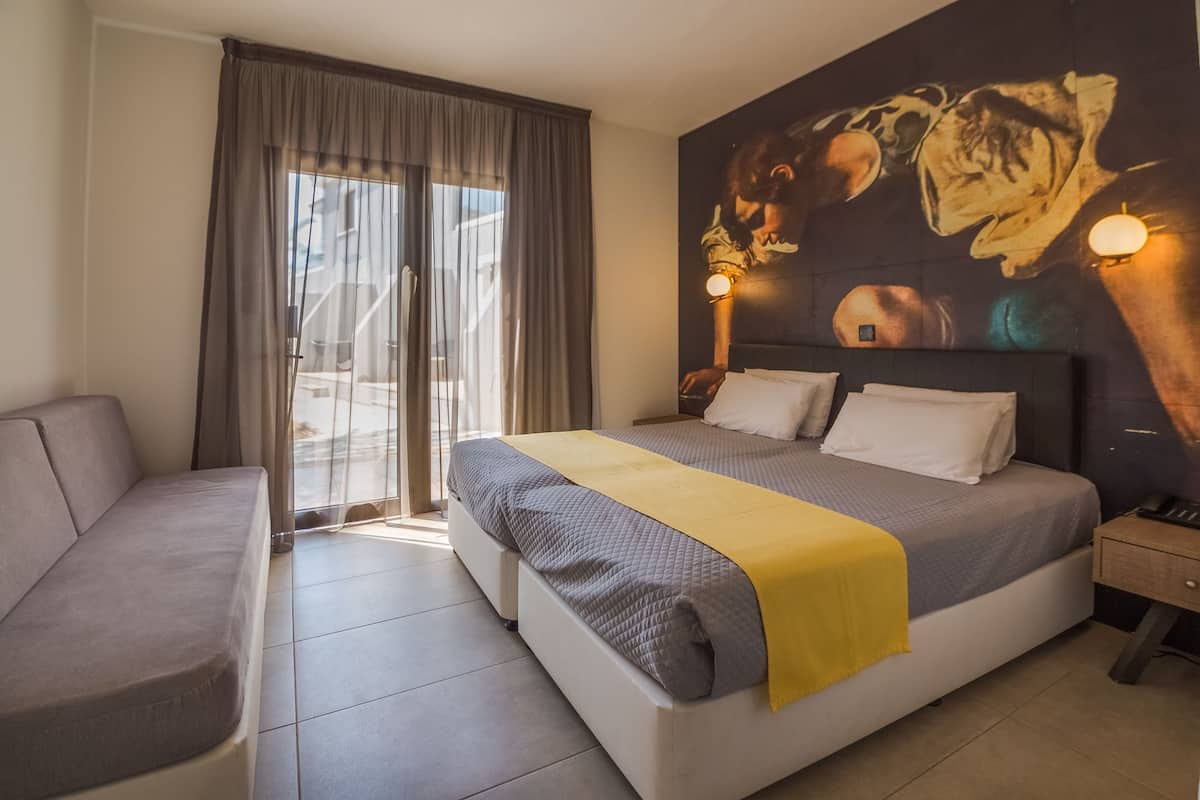 Ein Hotelzimmer mit Bett, einer Couch, einem großen Fenster mit Vorhängen und Wandbild.