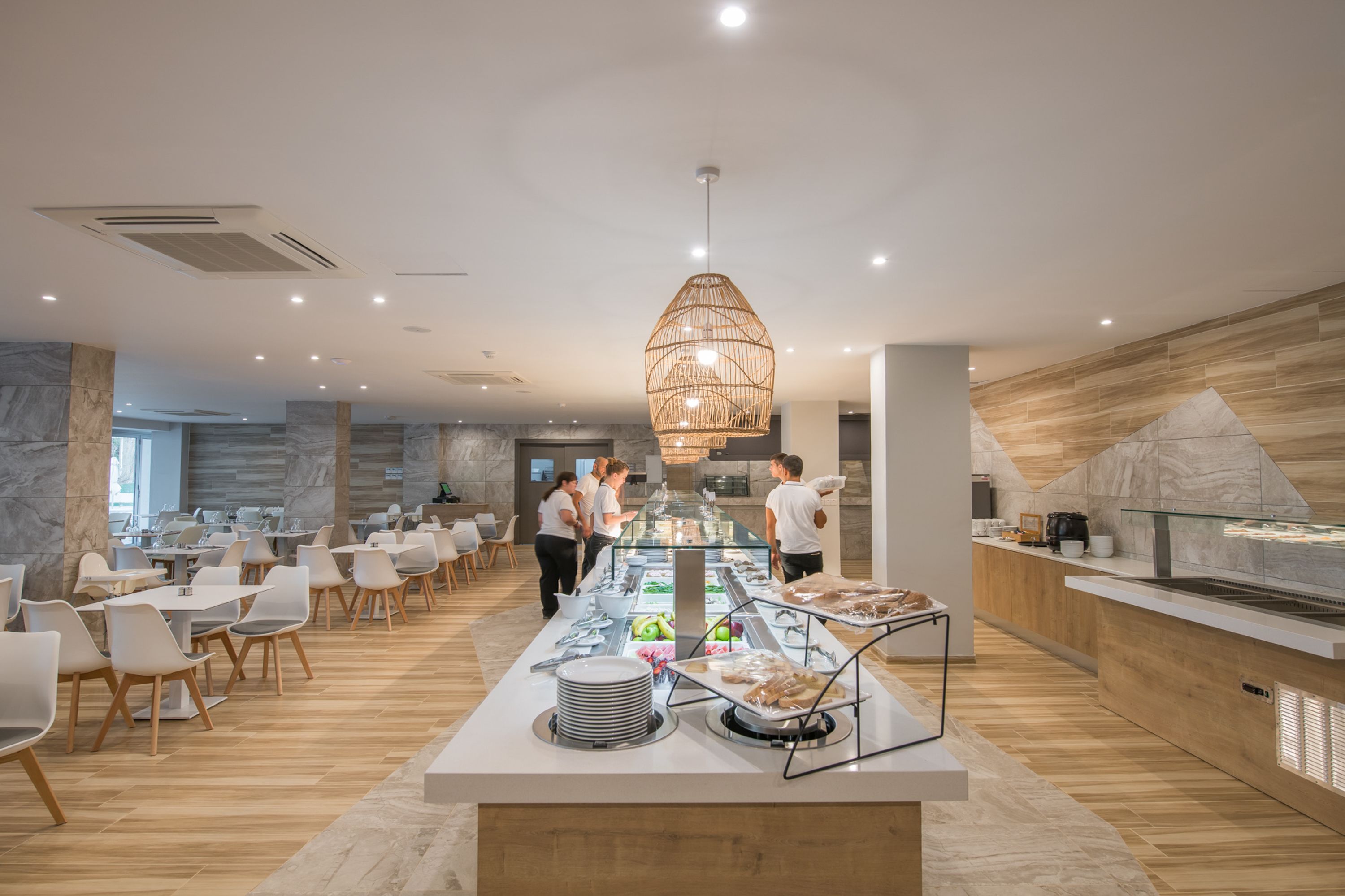 A modern restaurant with a buffet setup, marble walls, and a central hanging light fixture.