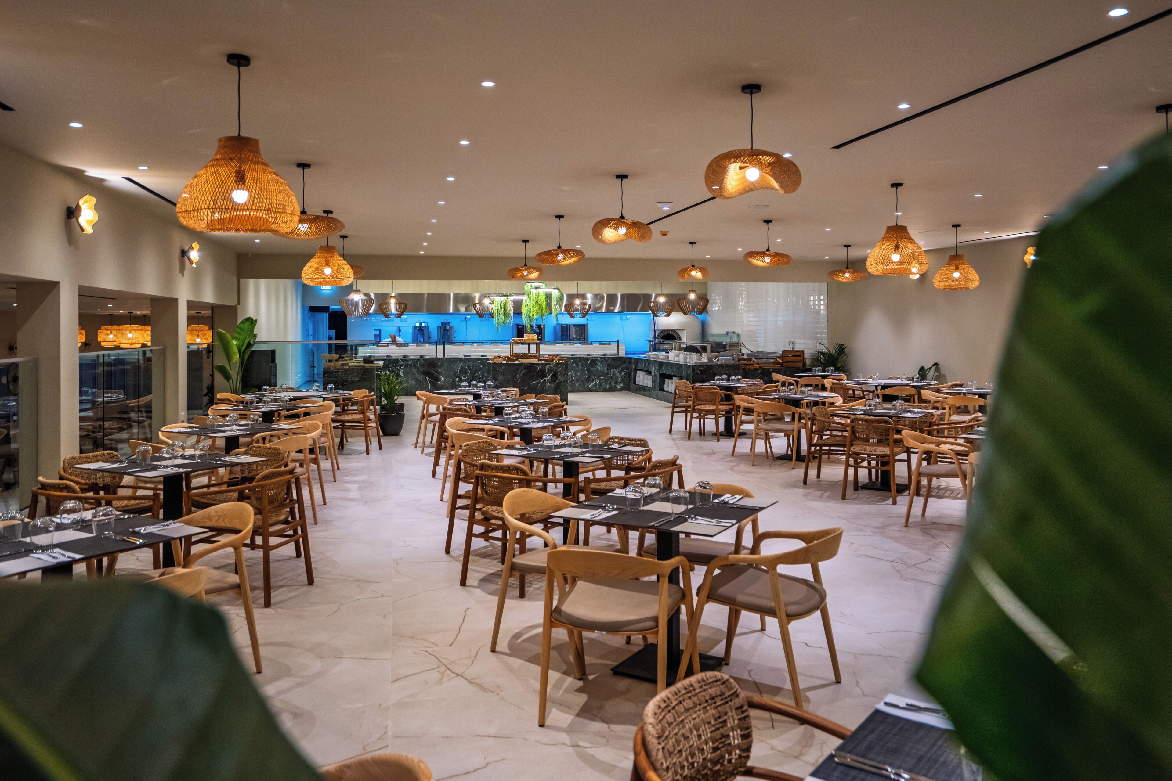 Ein Restaurant mit mehreren Tischen und Stühlen, hängenden Pendelleuchten und einer Küche im Hintergrund.