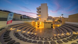 A circular seating area with a central structure, surrounded by a building with balconies. - Narcissos Waterpark Resort (Paralimni)