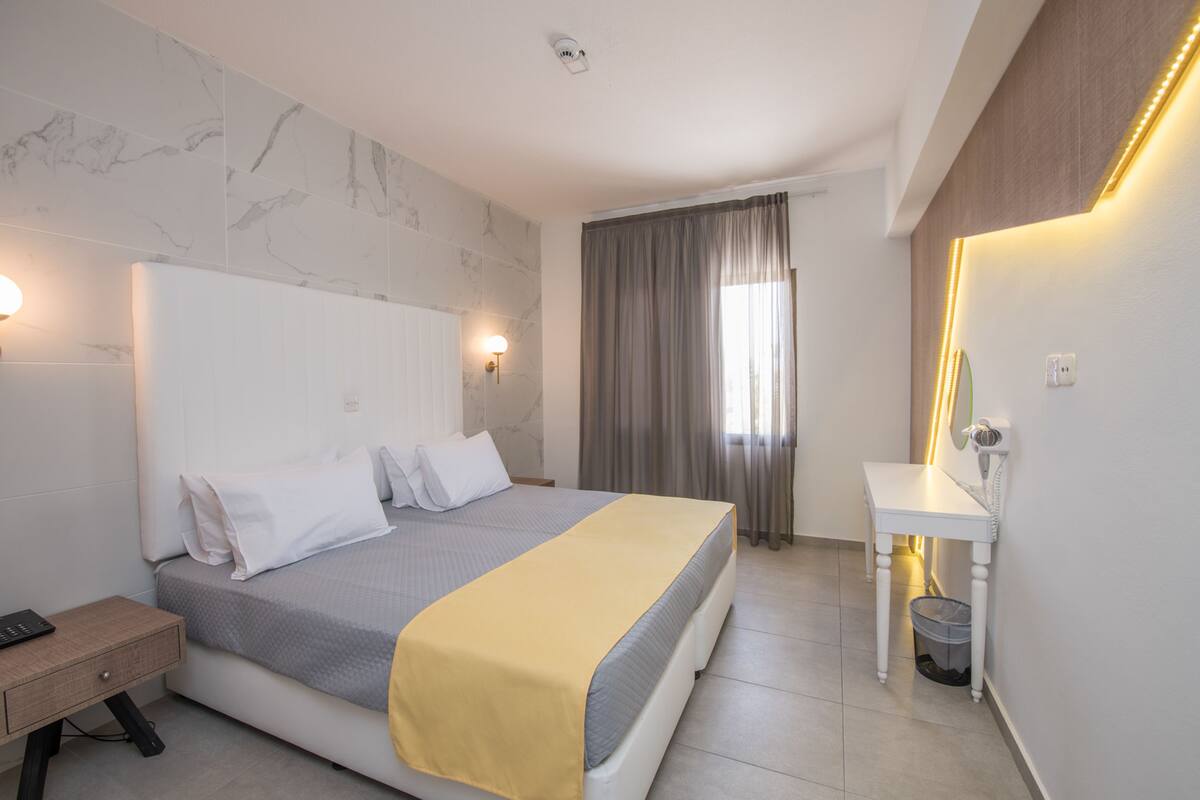 Ein Hotelzimmer mit Bett, Nachttisch und Schreibtisch mit Lampe.