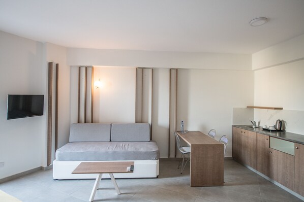 A compact living space with a sofa, a small dining table, a TV, and a kitchenette.