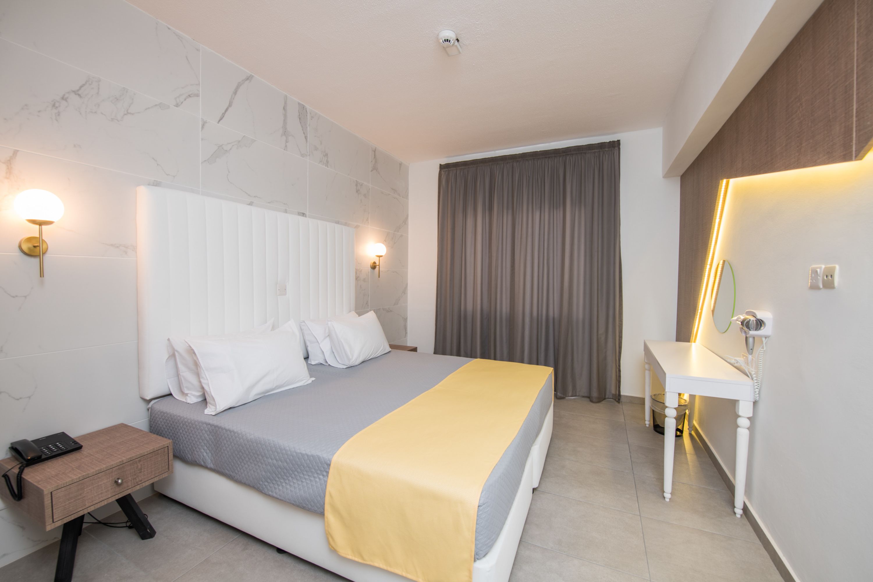 A modern hotel room with a bed, bedside table, and a mirror.