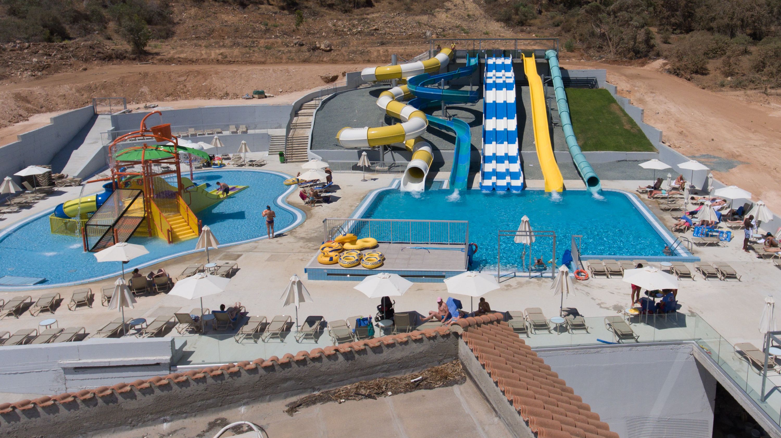 A water park with multiple slides and pools, surrounded by sun loungers and umbrellas.