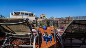 Terraço no telhado com duas cadeiras, uma mesa pequena com bandeja e vista para um edifício com cúpula verde.