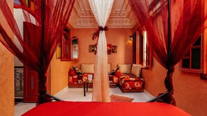 Um quarto com colcha vermelha, dois sofás com almofadas estampadas, um armário vermelho e teto decorativo.