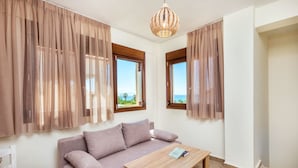 Ein Zimmer mit einer Couch, einem Holztisch und Meerblick durch zwei Fenster.
