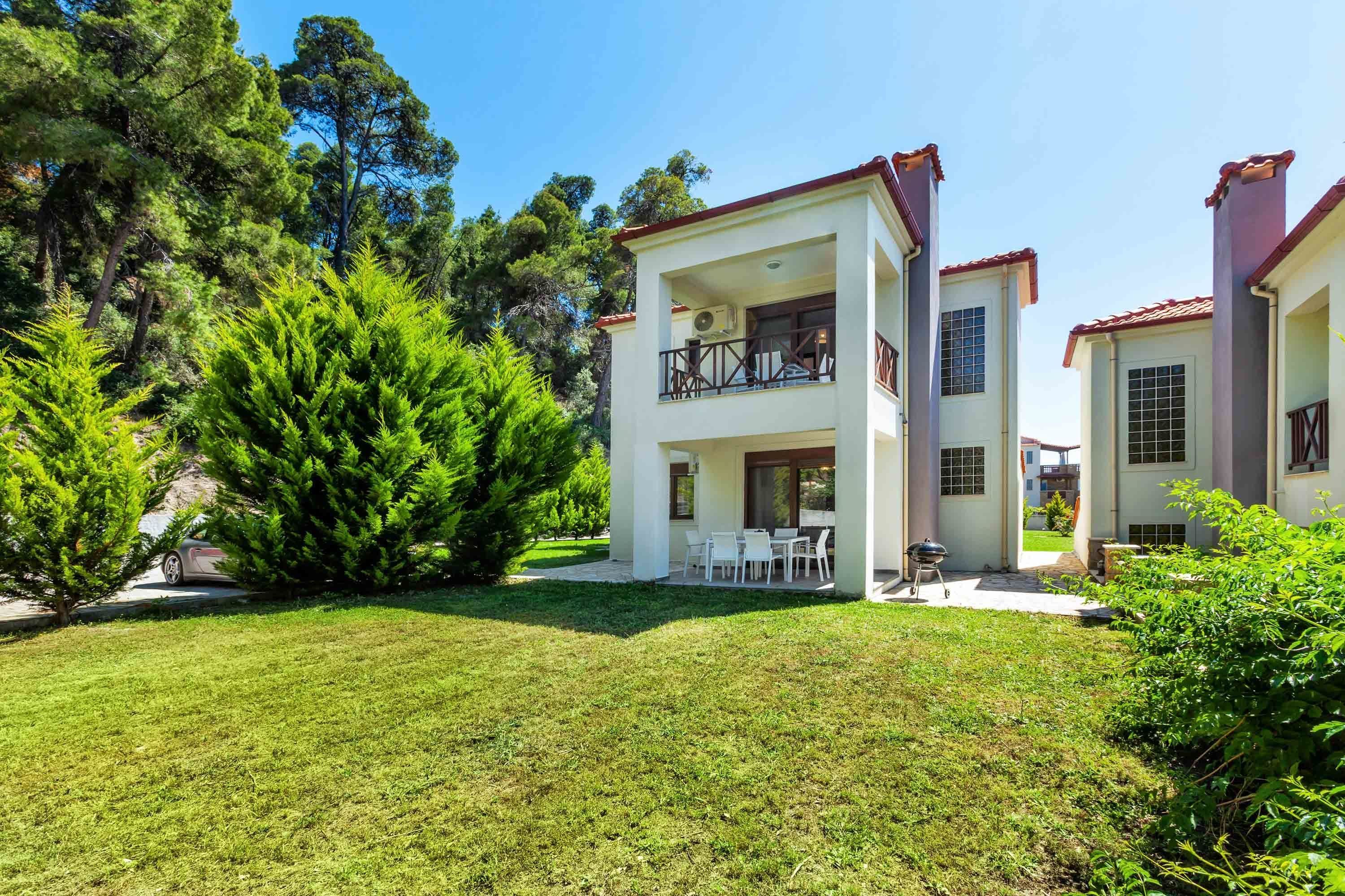 A two-story house with a balcony, a patio with outdoor furniture, and a well-maintained lawn.