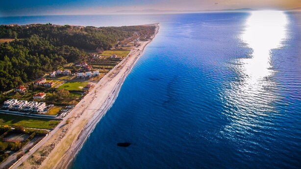 Ein Luftbild einer Küstenregion mit einem langen Strand, Wohnhäusern und einem dichten Waldgebiet.