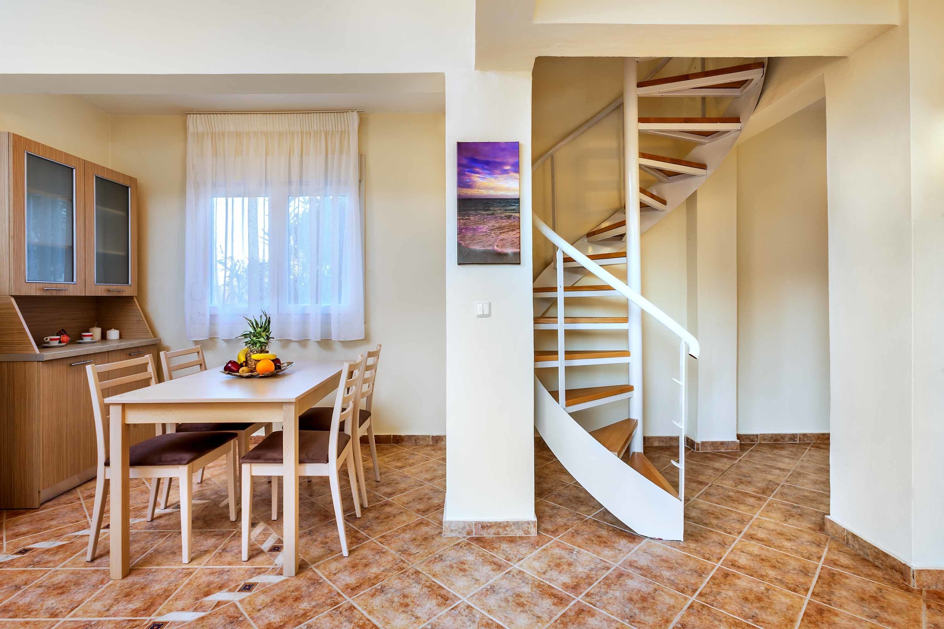 A dining area with a wooden table and chairs, a kitchen with cabinets, and a spiral staircase.