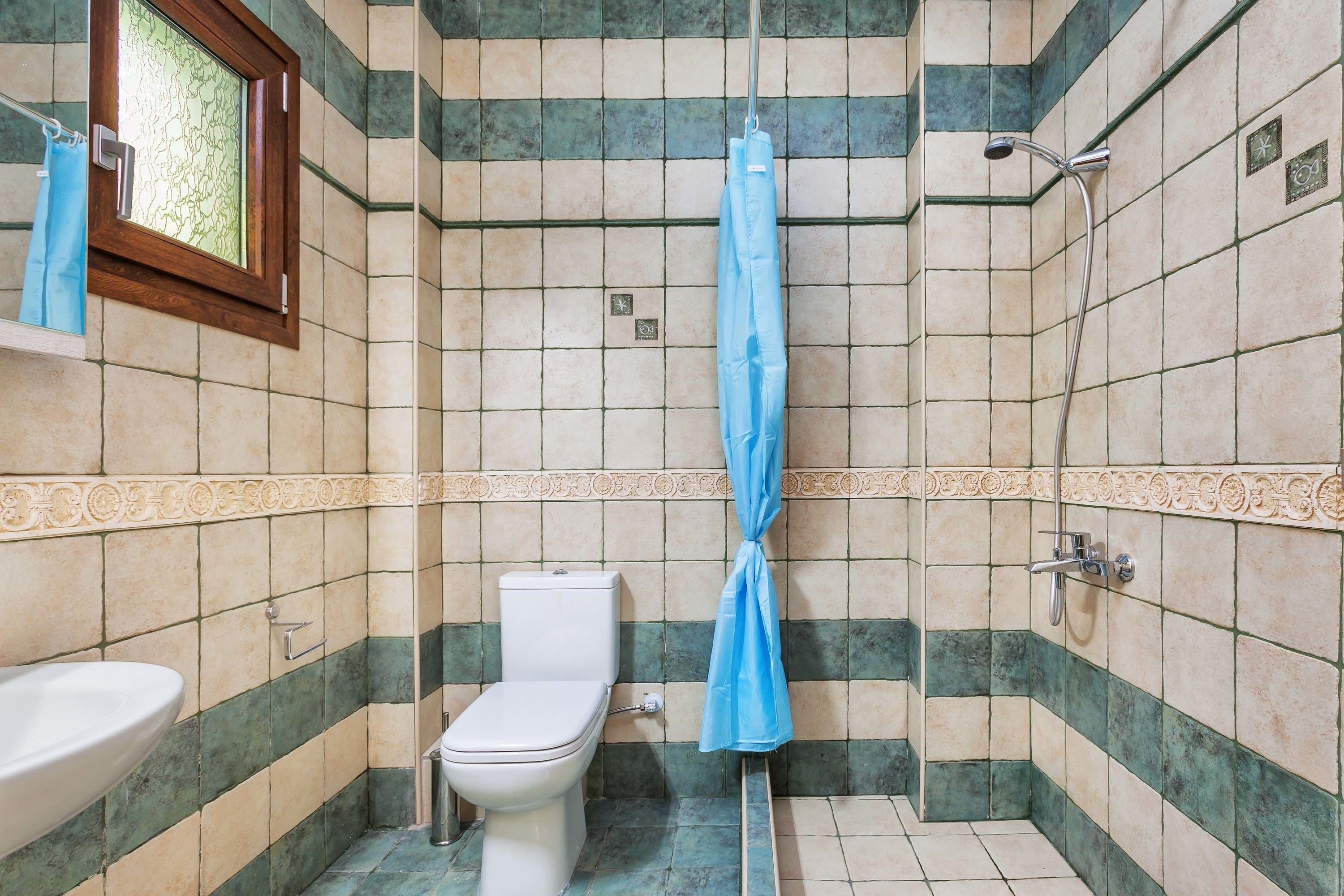 A bathroom with a toilet, sink, shower, and a window with a curtain.