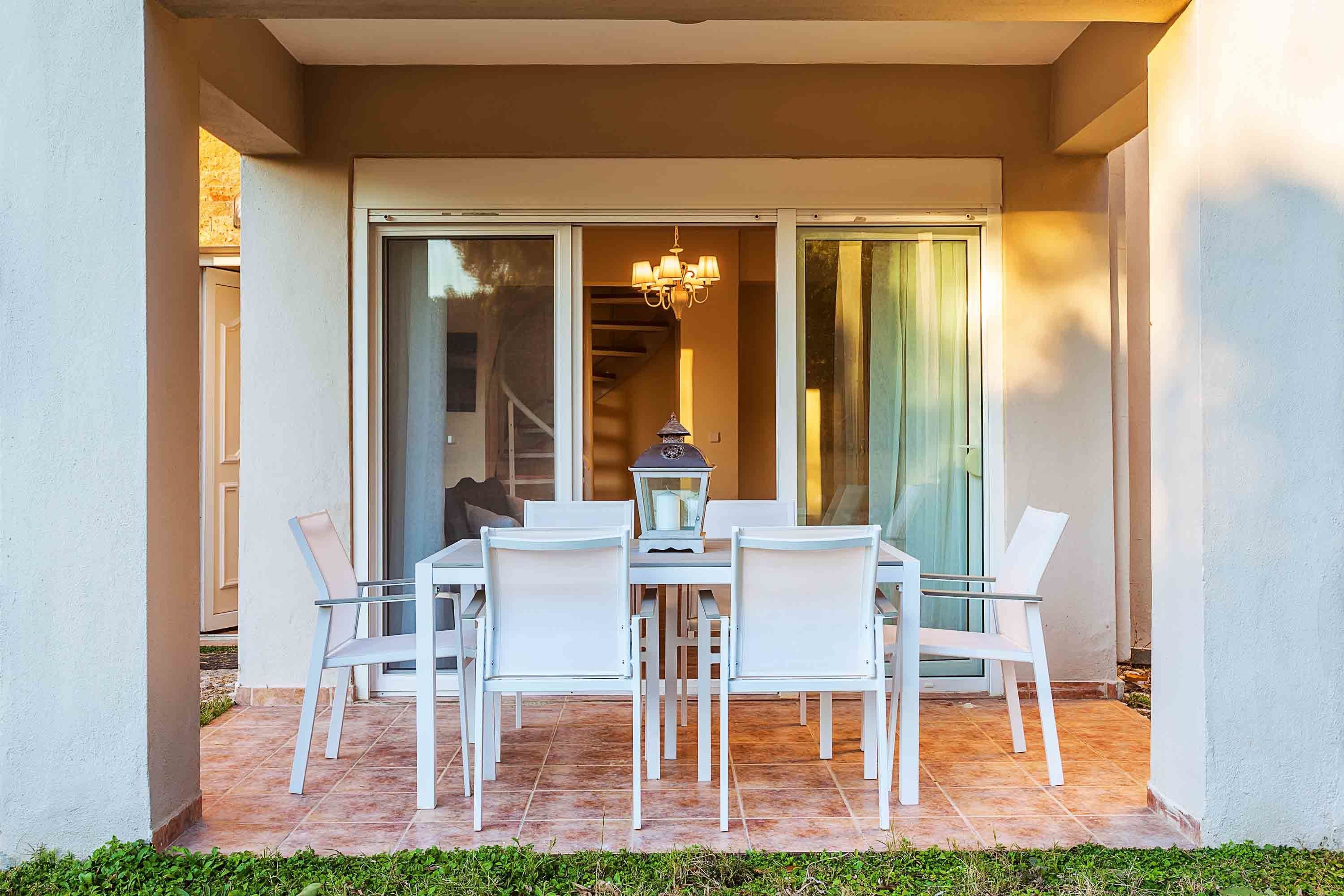 A patio with a table and chairs, a lantern, and a view of a staircase and interior through glass doors.