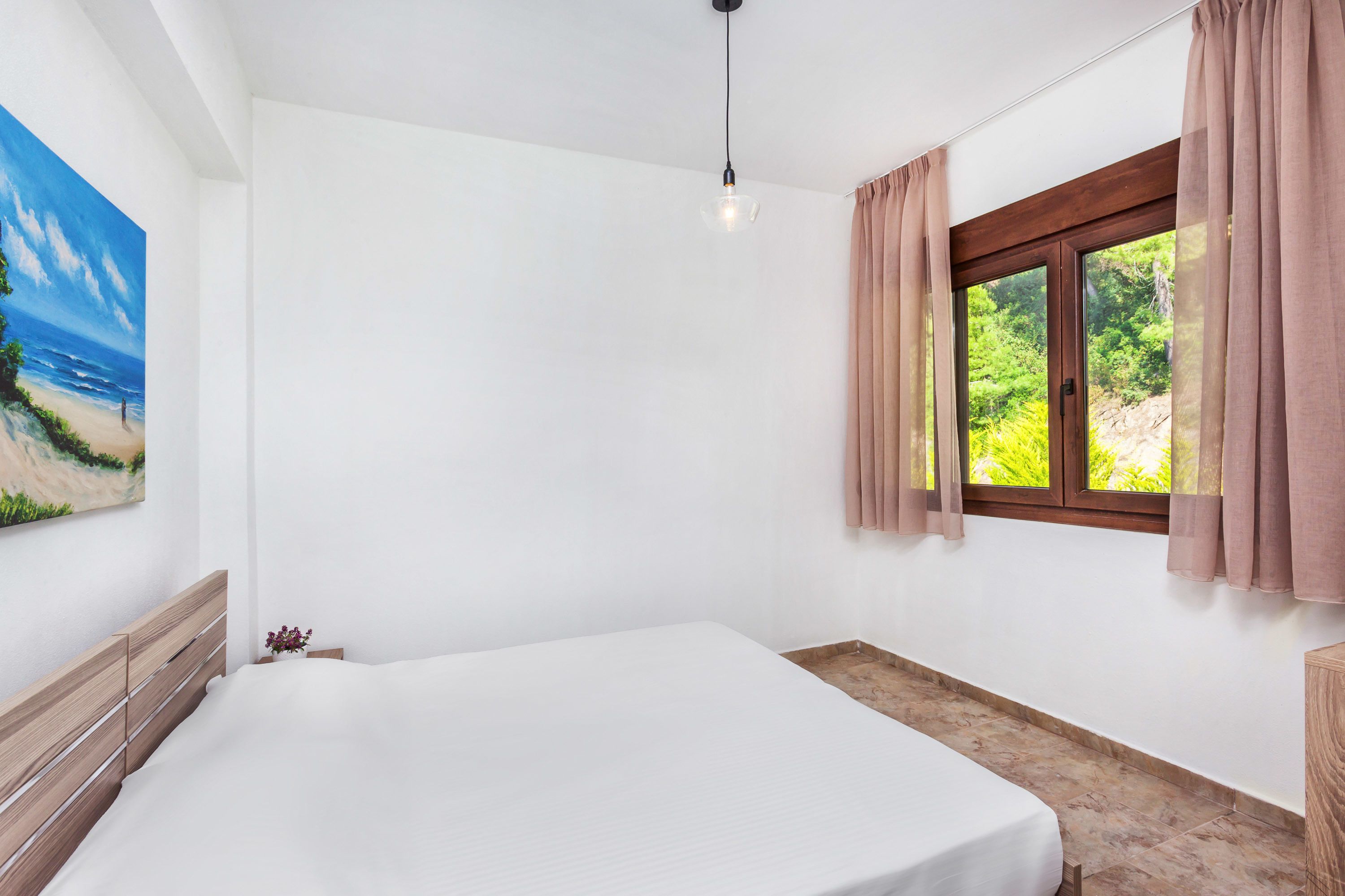 Ein Schlafzimmer mit Bett, einem Fenster mit Vorhängen, einem Bild an der Wand und einer Pendelleuchte.
