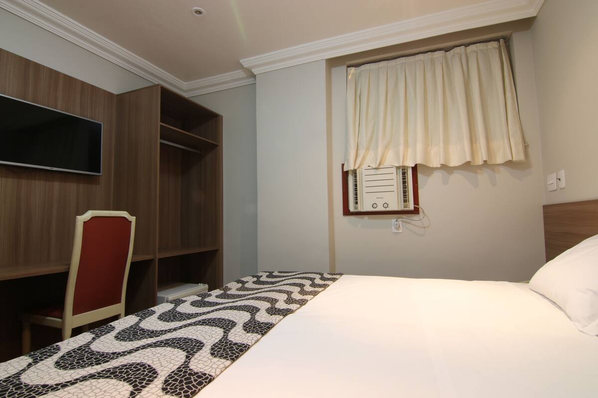 Une chambre d’hôtel comprenant un lit, un téléviseur fixé au mur, une fenêtre avec des rideaux et une armoire intégrée.