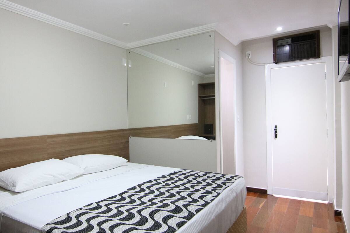 Une chambre à coucher avec un lit, un grand miroir, une armoire et une petite fenêtre.