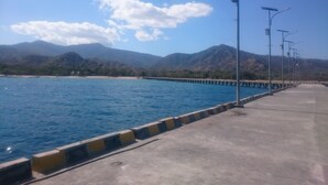 A coastal road with a concrete barrier, street lamps, and a clear blue sky. - Laislabonita (Labuan Bajo)