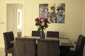 Uma área de refeições com mesa e cadeiras, um vaso com flores e um quadro na parede.