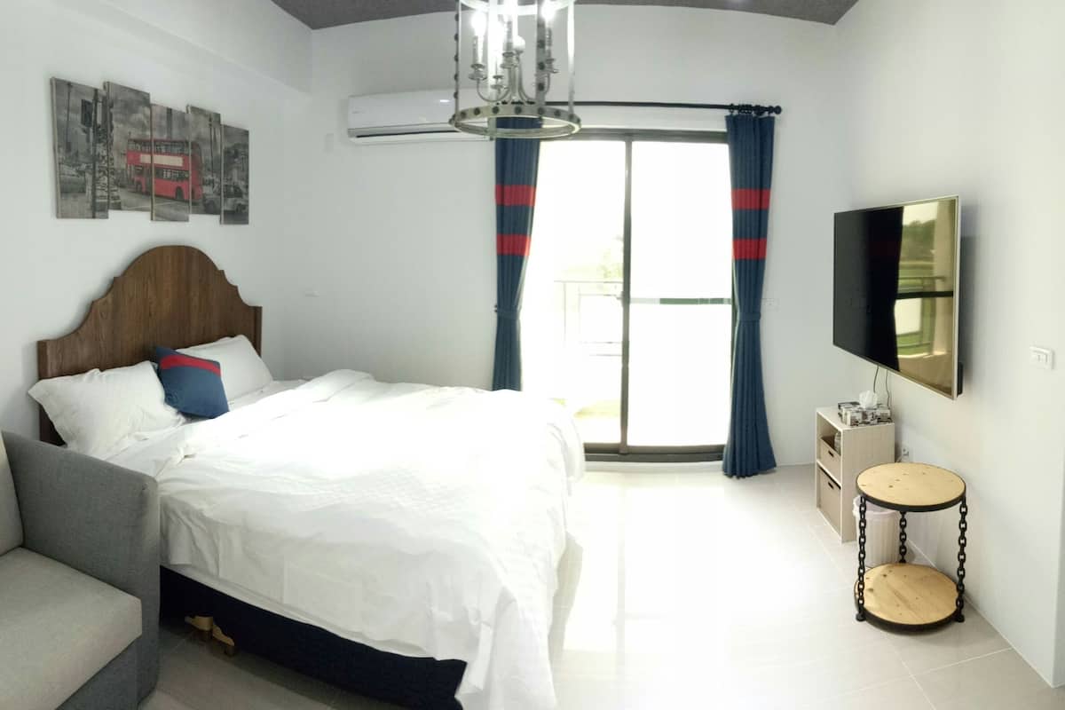 A hotel room with a bed, a TV, a ceiling light, and a window with curtains.