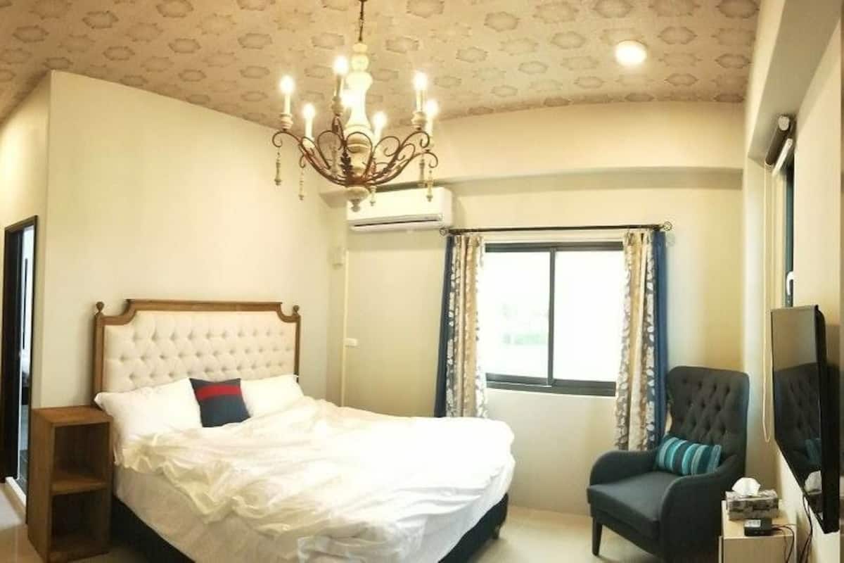 A bedroom with a bed, a chair, a TV, and a window with curtains.