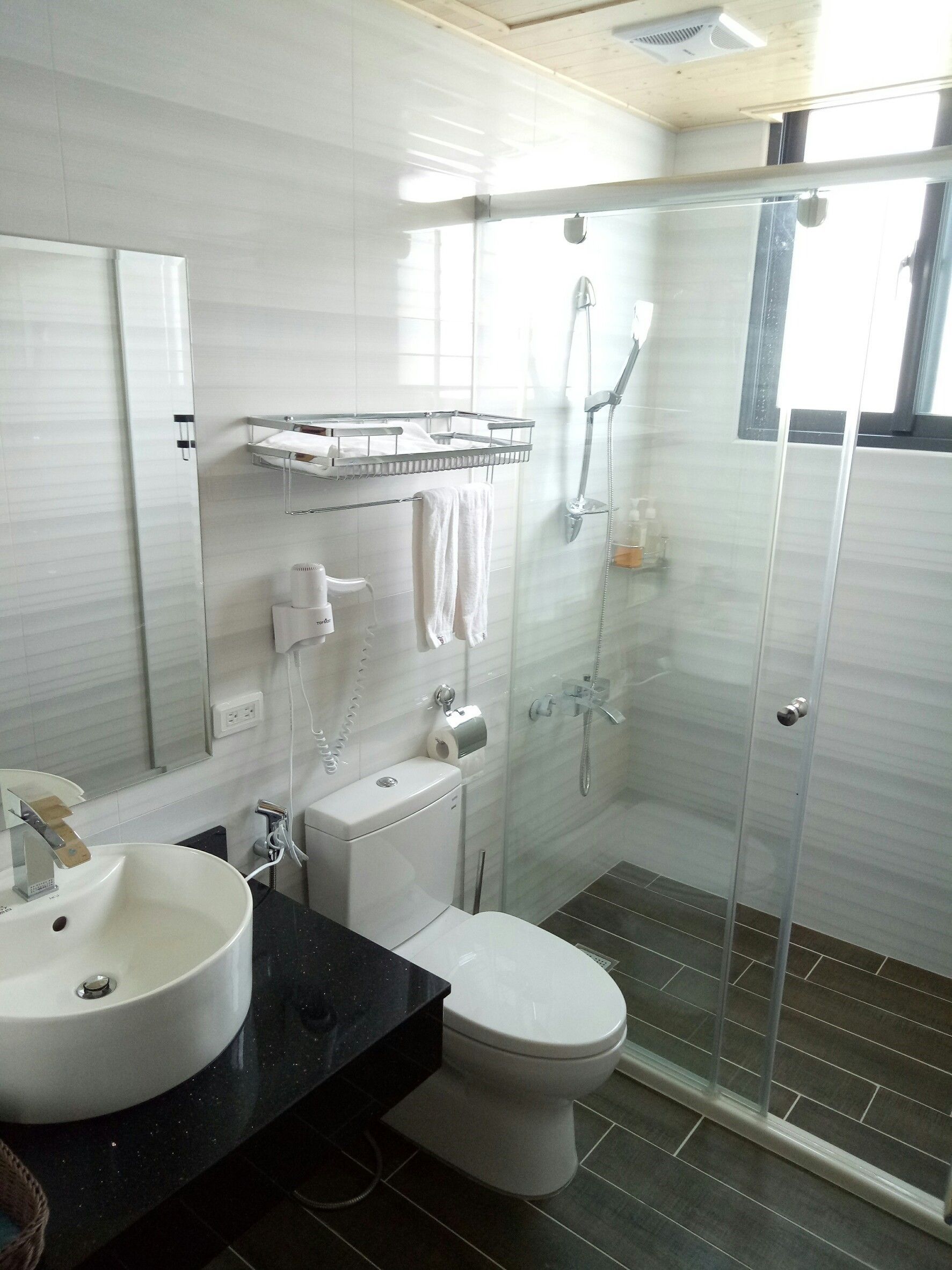 Un baño moderno con ducha de vidrio, lavamanos blanco y retrete.