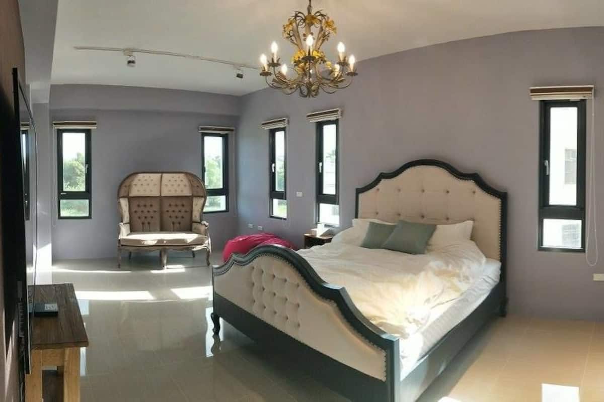 A bedroom with a large bed, a chair, and a chandelier.